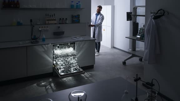 An ExpertLine laboratory washer positioned in a dark laboratory and the chamber lighting shining brightly.