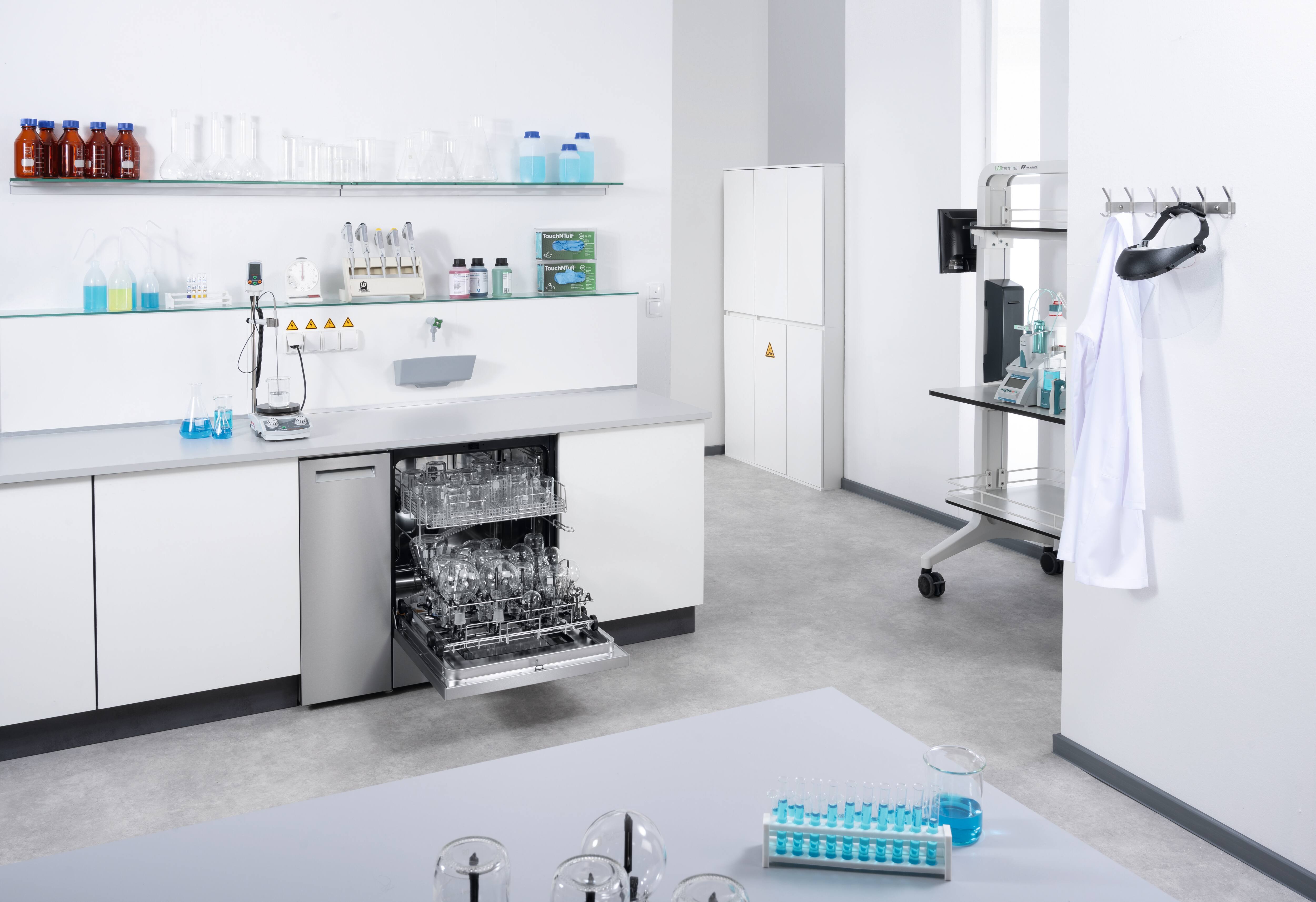 A 90 cm ExpertLine laboratory washer with an open side compartment where two cleaning agent canisters are connected.