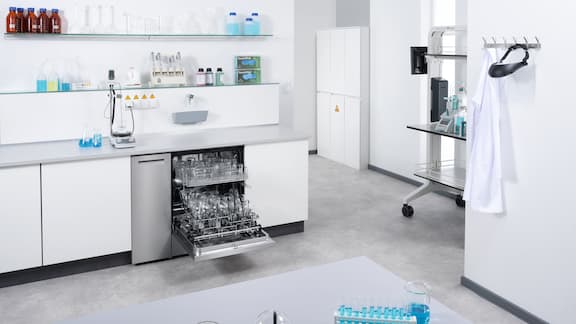 A 90 cm ExpertLine laboratory washer with an open side compartment where two cleaning agent canisters are connected.