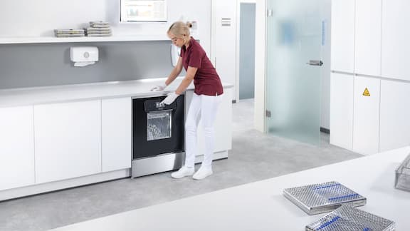 Asystentka stomatologiczna otwiera termodezynfektor ExpertLine w pomieszczeniu do reprocesowania