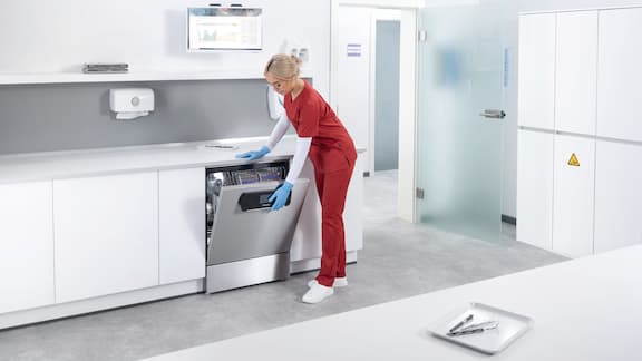 Asystentka stomatologiczna otwiera termodezynfektor Miele Professional ExpertLine w pomieszczeniu do reprocesowania