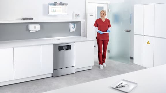 Dental assistant walks inside reprocessing room holding a tray