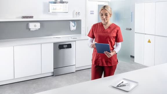 A dental assistant looks at a tablet in an instrument reprocessing room
