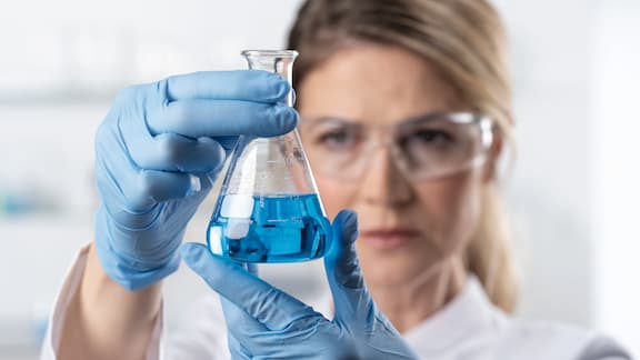 A lab technician testing a blue liquid in an Erlenmeyer flask.