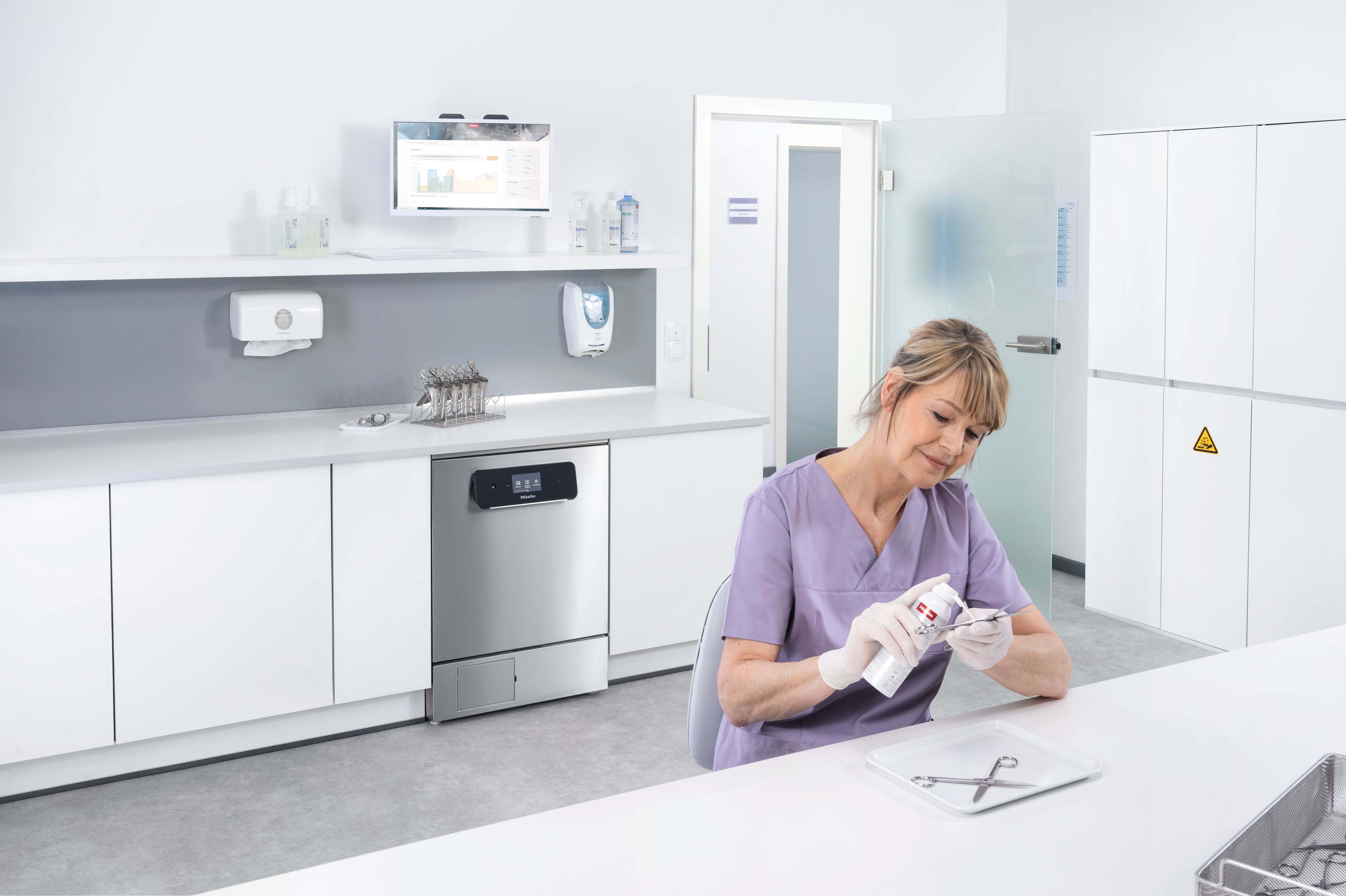 Een medisch assistent behandelt instrumenten met ProCare-chemicaliën van Miele Professional. Op de achtergrond staat een Miele Professional PWD 8682 ExpertLine reinigings- en desinfectieapparaat van roestvrij staal.