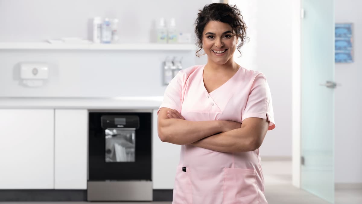 Een tandarts in roze kleding, met de ExpertLine met glazen deur op de achtergrond