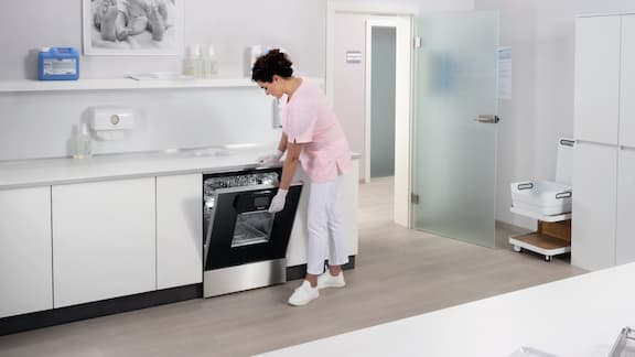 Une assistante médicale ouvre un laveur-désinfecteur Miele dans une salle de préparation des instruments.