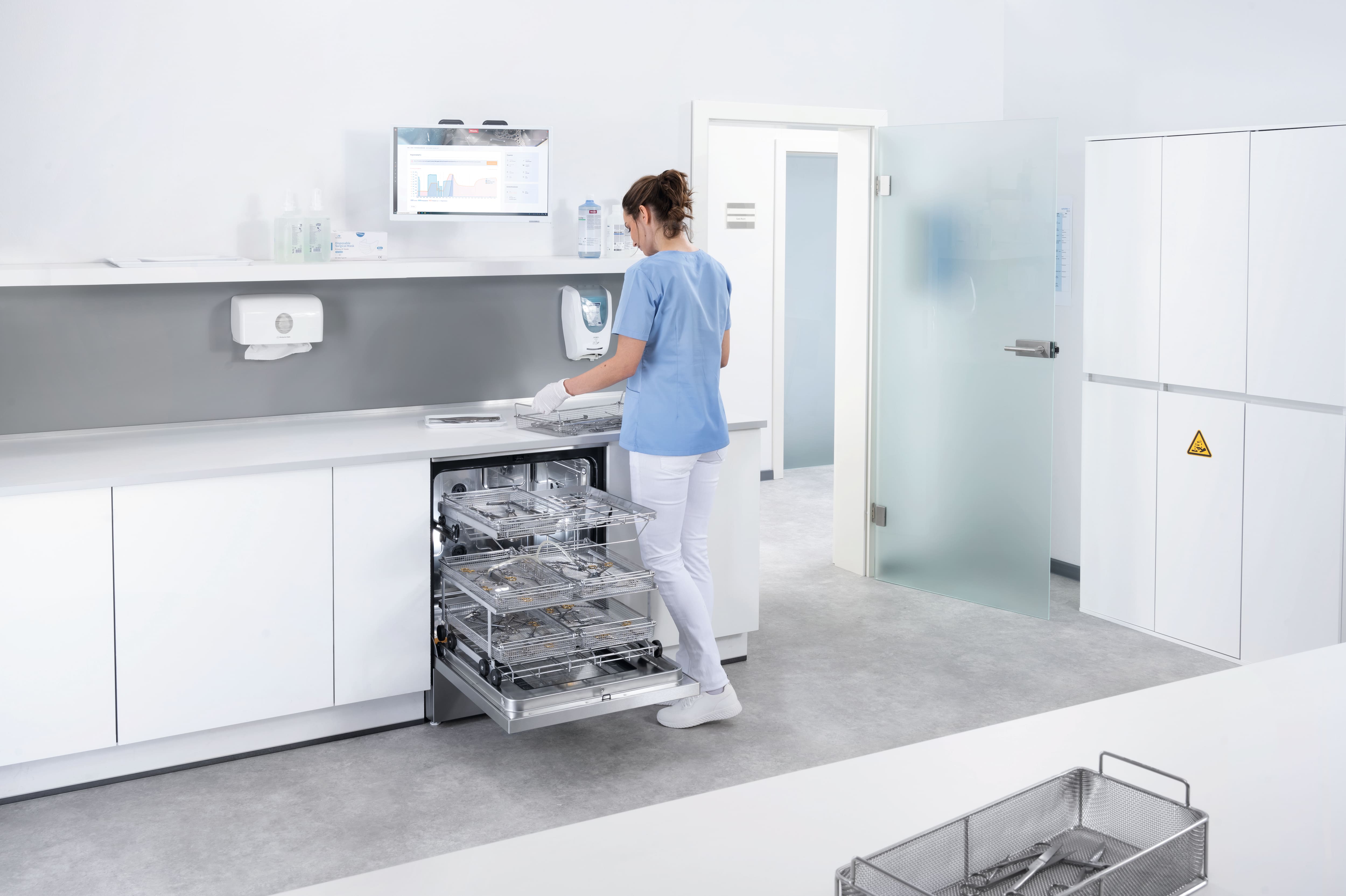 A dental assistant works in the instrument reprocessing room with an ExpertLine machine.