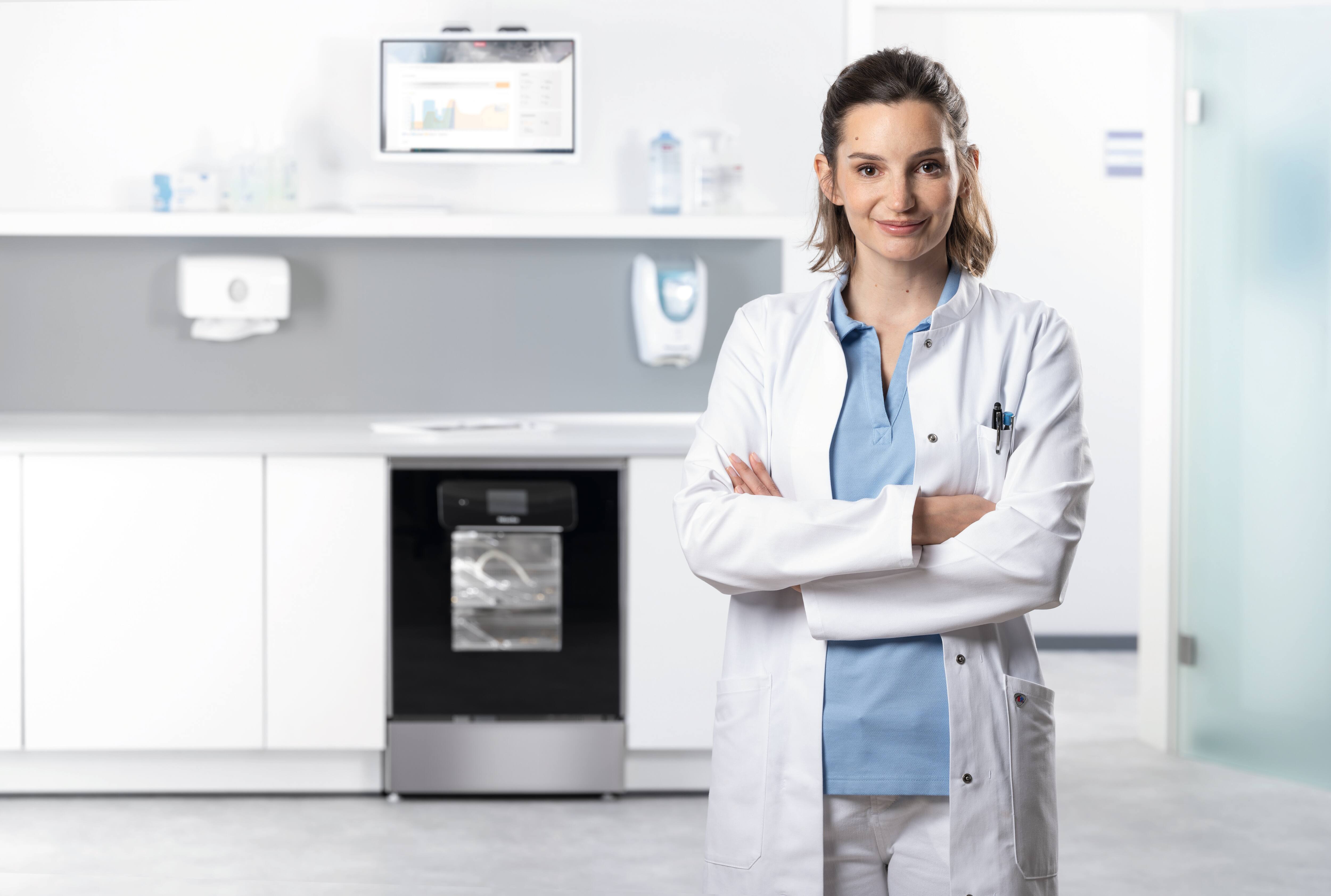 Lékař se usmívá do objektivu kamery v místnosti pro přípravu instrumentů s mycím a dezinfekčním automatem řady ExpertLine