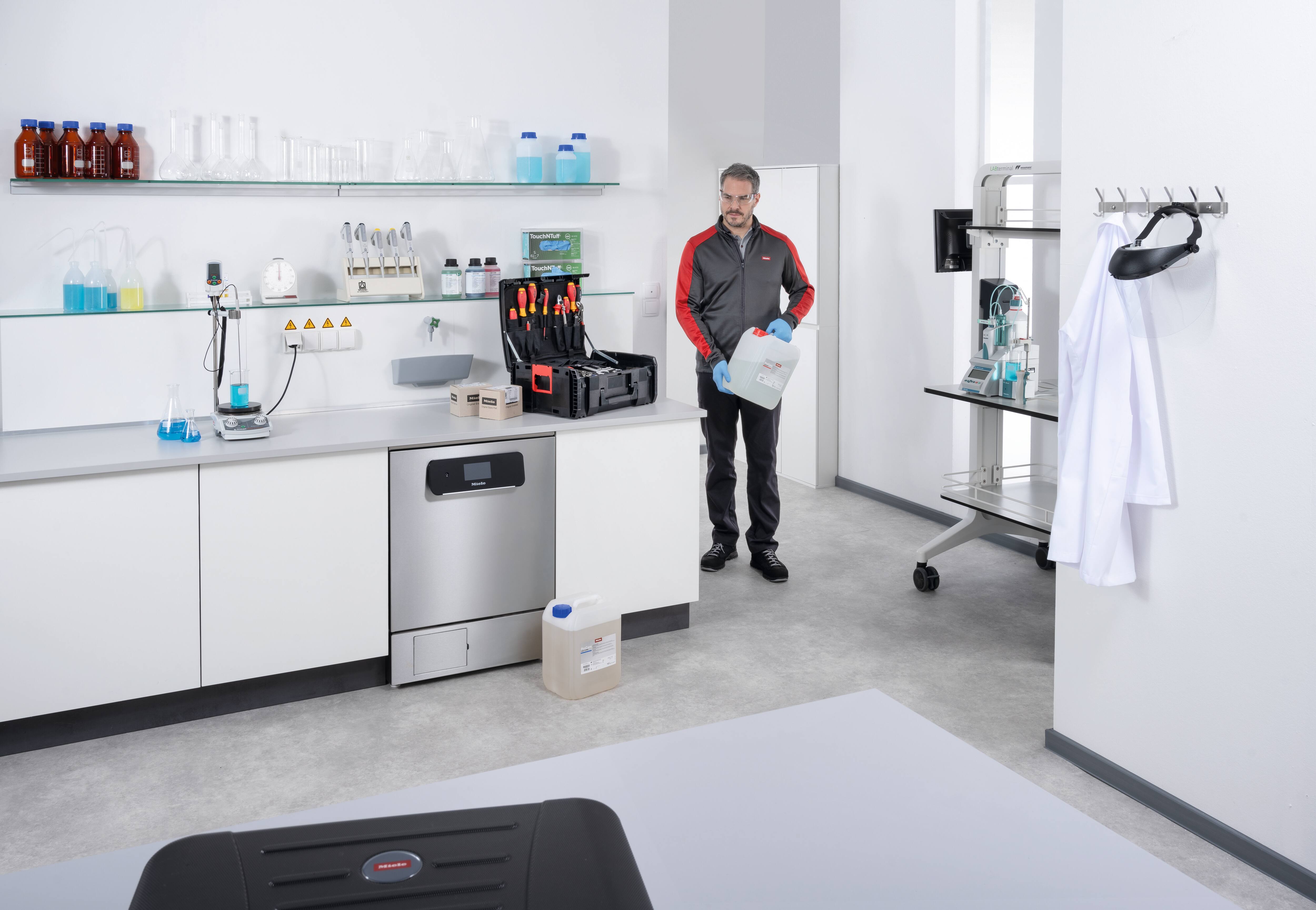 Ein Kundendiensttechniker geht in ein Labor mit einem ProCare Lab Reinigungsmittelkanister in der Hand.