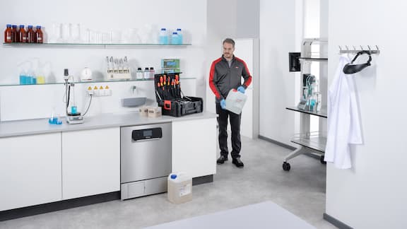 Technik serwisowy wchodzący do laboratorium z kanistrem detergentu ProCare Lab w ręku.