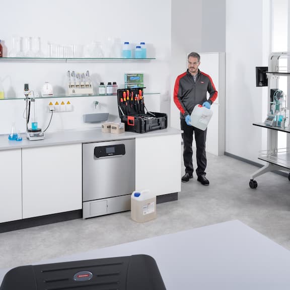 A service technician entering a laboratory with a ProCare Lab cleaning agent canister in his hand.