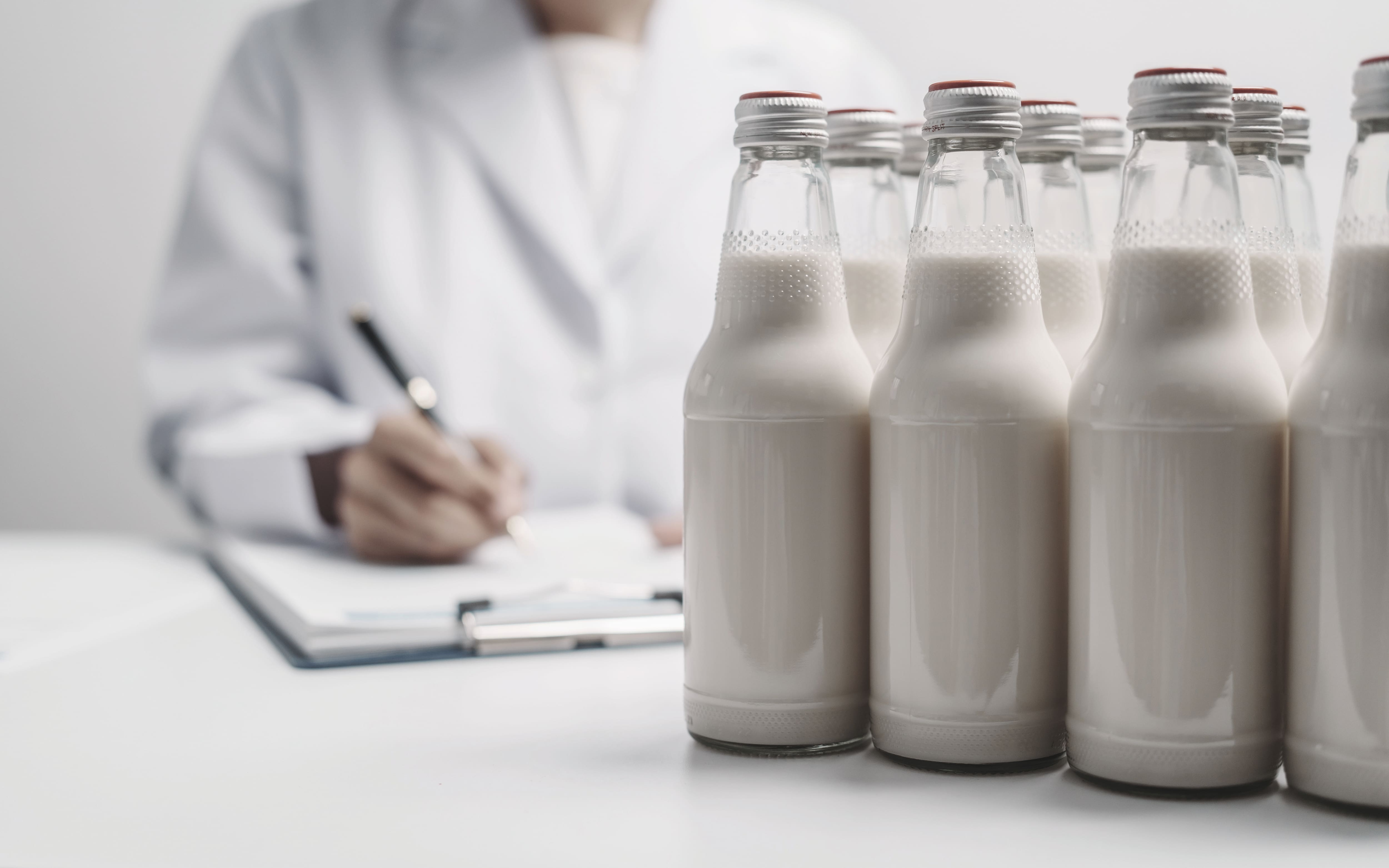 Mehrere Flaschen mit abgefüllter Milch stehen auf einem Tisch und ein Labormitarbeiter macht Notizen,.