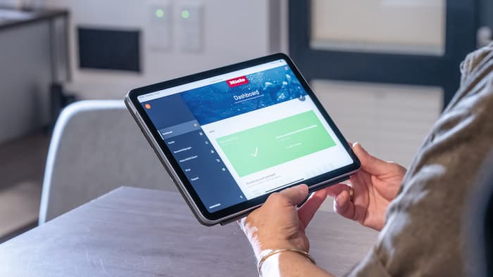 Jemand hält ein Tablet, es zeigt das Dashboard von Miele MOVE Connect.