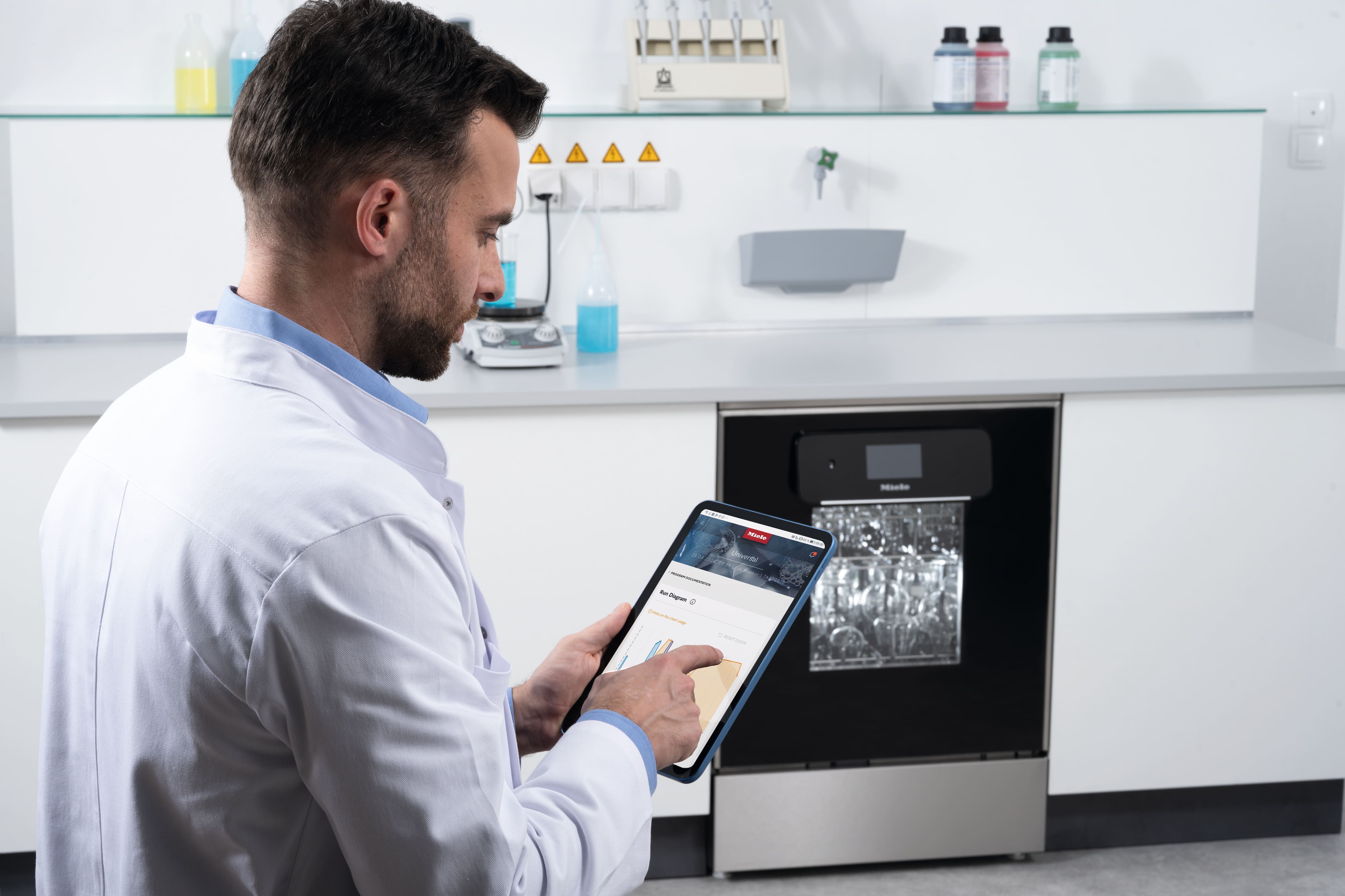 Labormitarbeiter bedient ein Tablet zur Überprüfung eines Laborspülers.