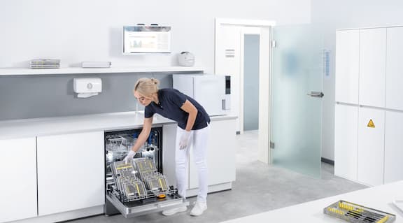 Asystentka stomatologiczna ładuje termodezynfektor Miele Professional narzędziami stomatologicznymi w pomieszczeniu do reprocesowania.