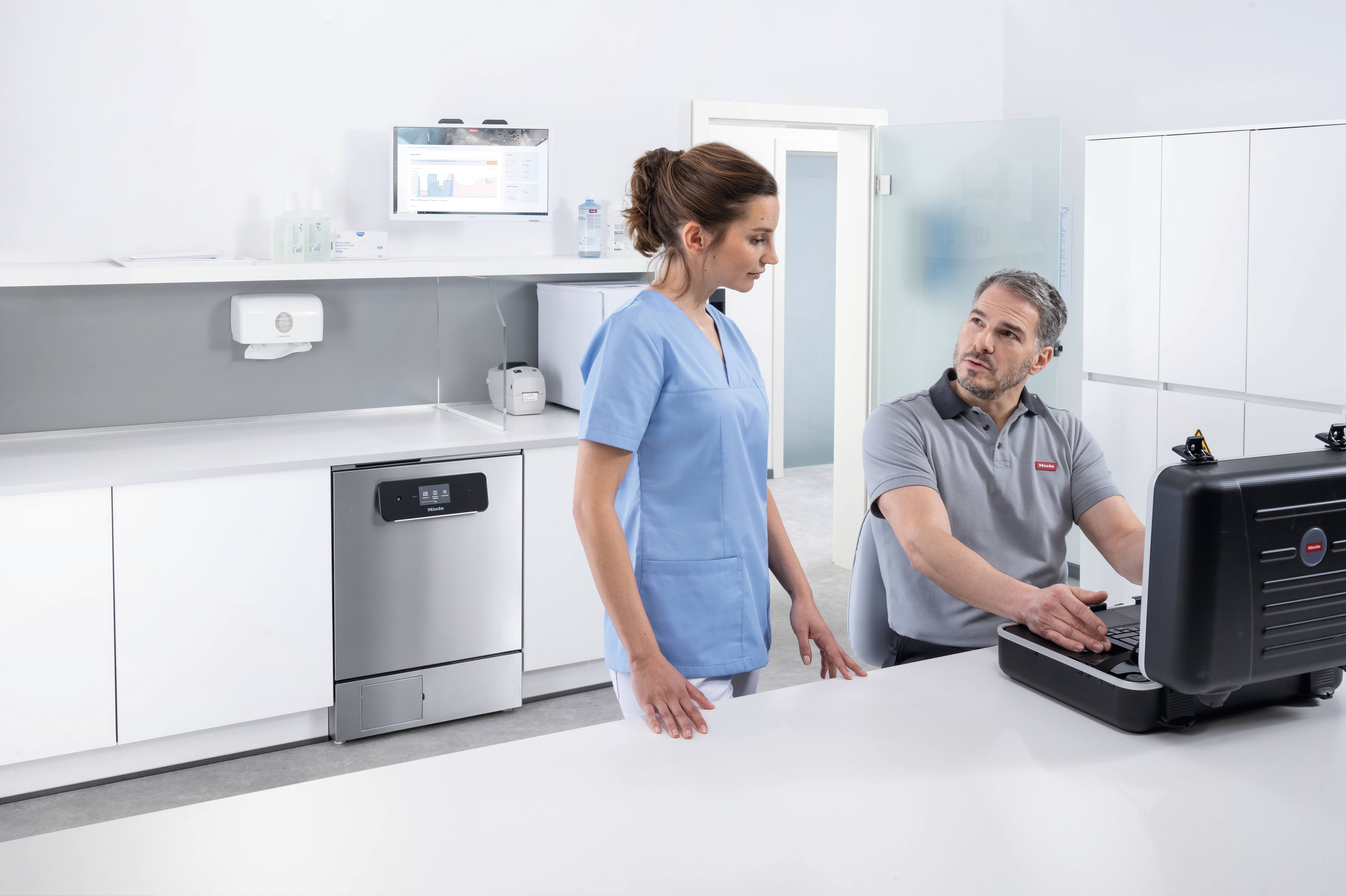 Servis teknisyeni küçük sterilizatörün önünde doktor asistanı ile konuşuyor.