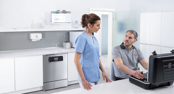 Servis teknisyeni küçük sterilizatörün önünde doktor asistanı ile konuşuyor.