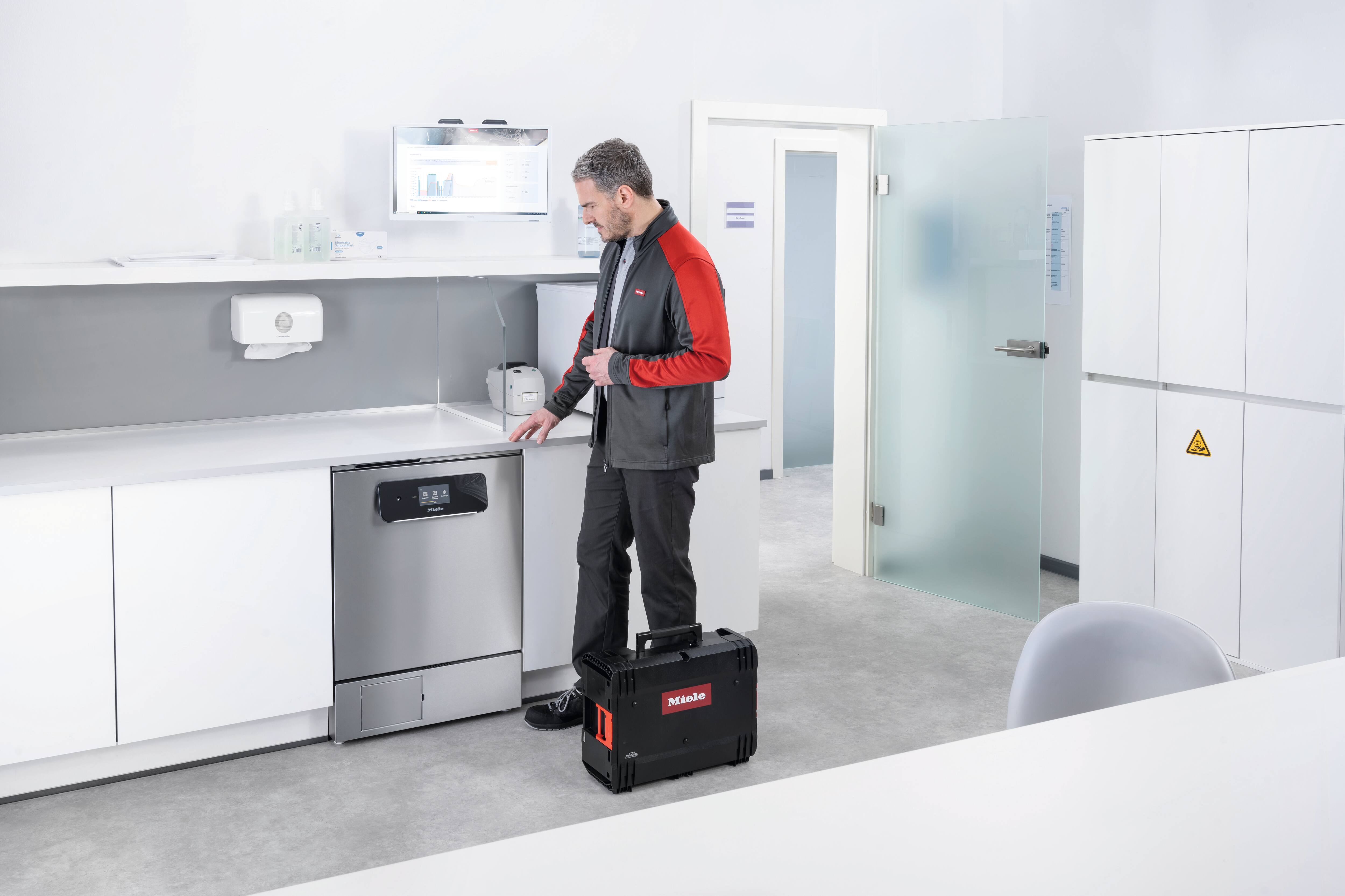 Ein Miele Service Mitarbeiter steht vor seinem Van mit geöffneter Seitentür und lächelt in die Kamera. 