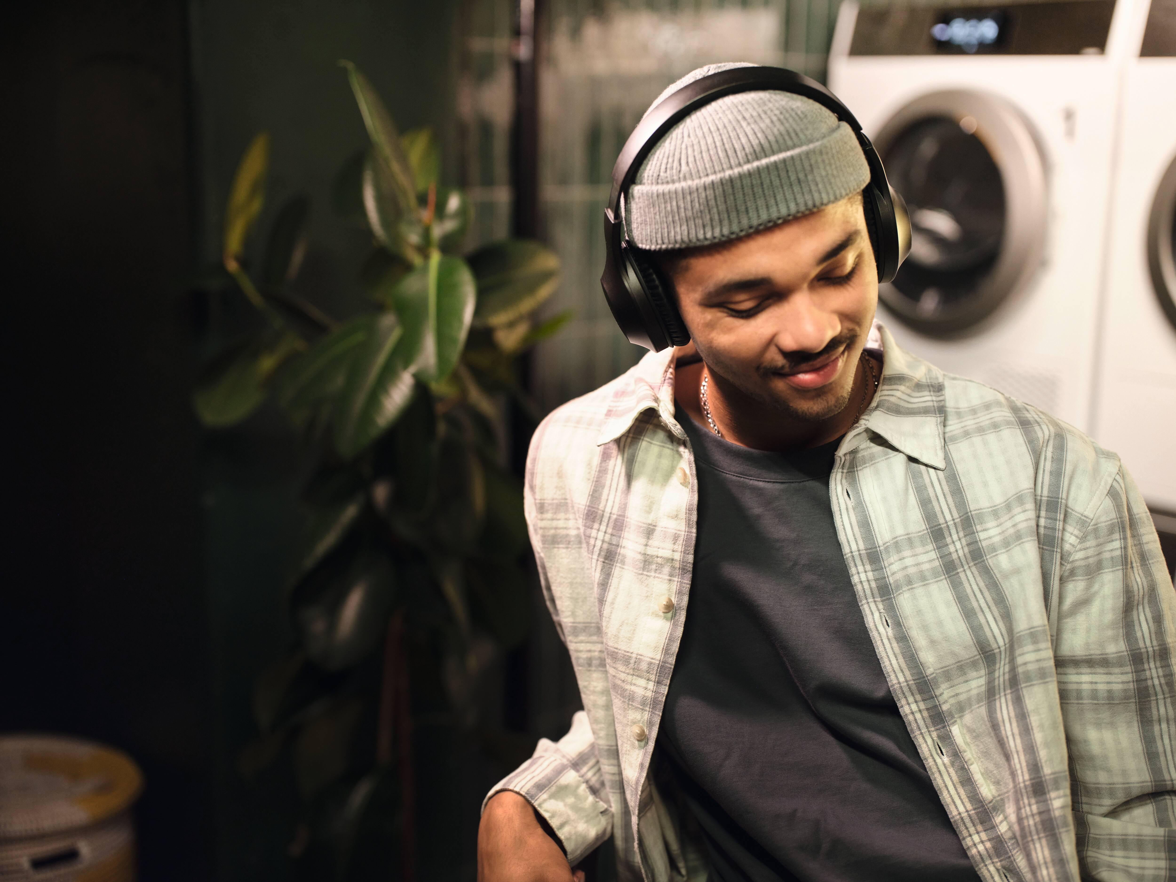 Ein junger Student hört entspannt und mit geschlossenen Augen Musik auf seinen Kopfhörern. Im Hintergrund sieht man einen Miele Professional Kleine Riesen Trockner.
