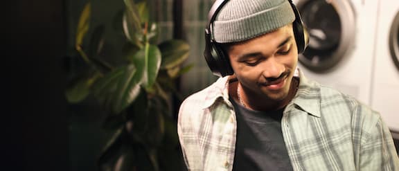 A young student relaxes and listens to music on his headphones with his eyes closed. In the background, there is a Miele Professional Little Giants tumble dryer.