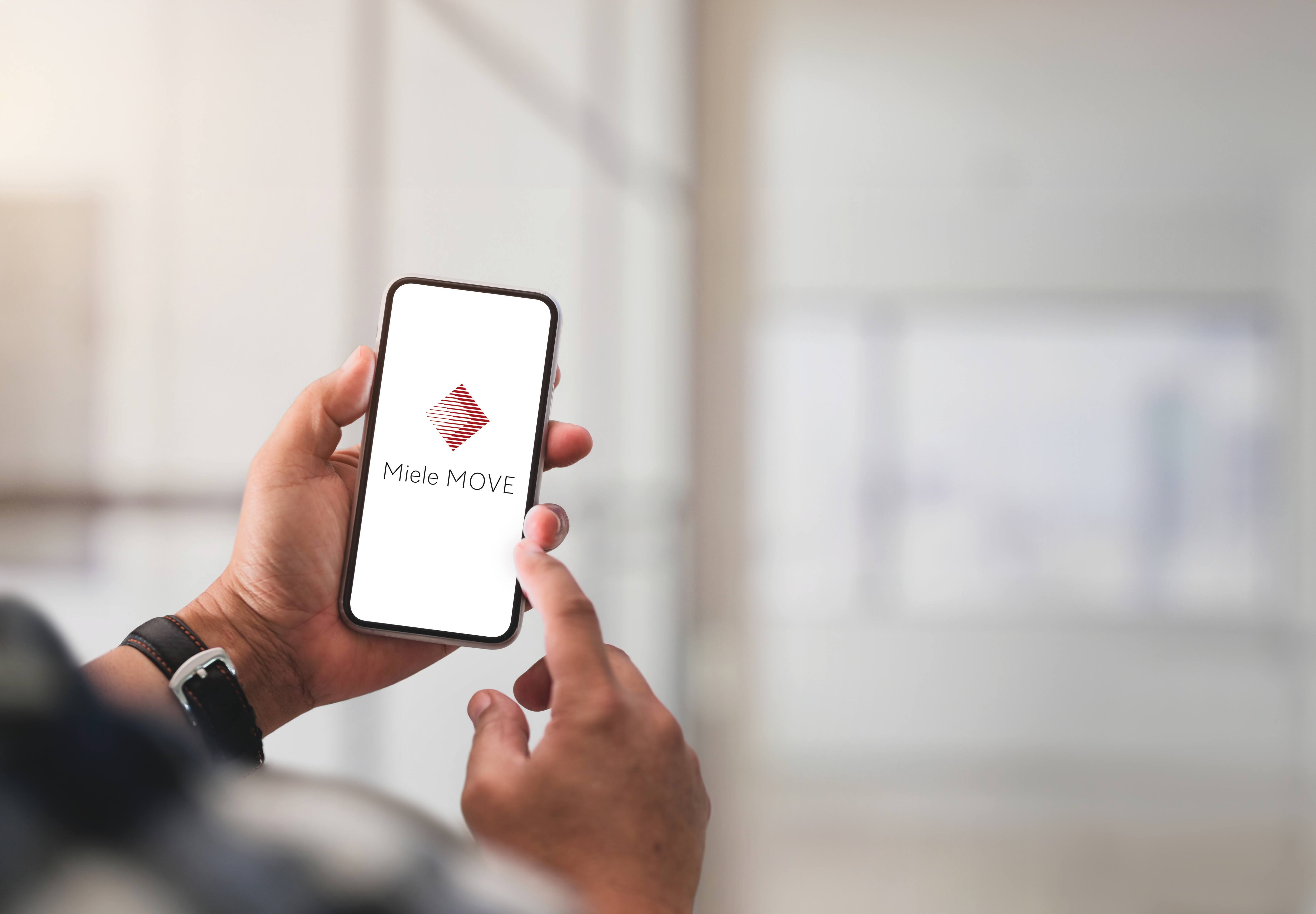 Una persona sujetando un móvil. En la pantalla se muestra la aplicación Miele MOVE connect. 