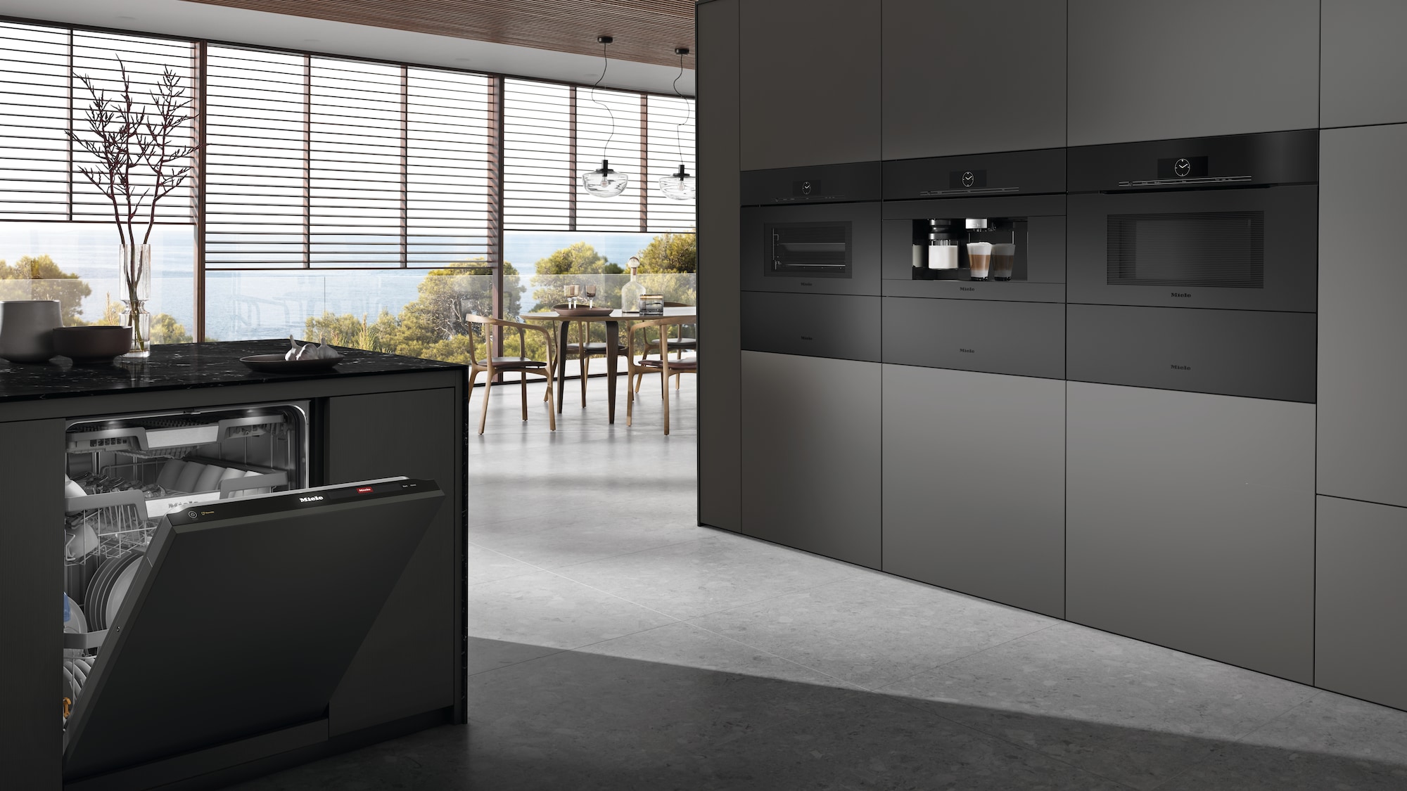 Modern kitchen with sleek dark cabinetry, built-in appliances, an open dishwasher, and large windows overlooking a scenic view with trees and a dining area.