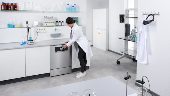 Pracownica laboratorium zamyka załadowaną podblatową zmywarkę laboratoryjną.