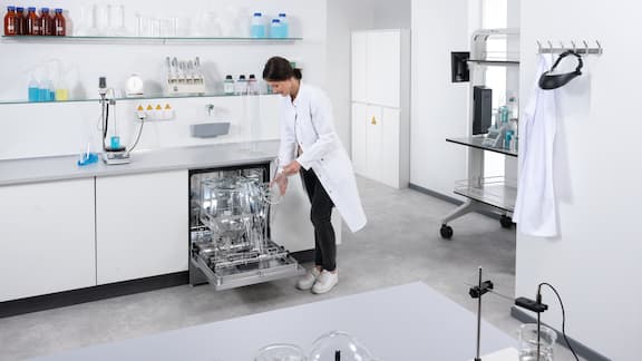 Une employée de laboratoire charge un lave-vaisselle de laboratoire sous évier Miele avec une fiole jaugée dans une salle de laboratoire.