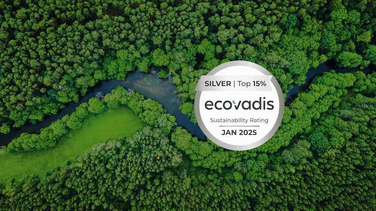 Luftfoto af en tæt skov med en flod, der snor sig gennem det grønne. I midten af billedet er der et rundt EcoVadis-logo med teksten »SILVER | Top 15% ecovadis Sustainability Rating JAN 2025«.