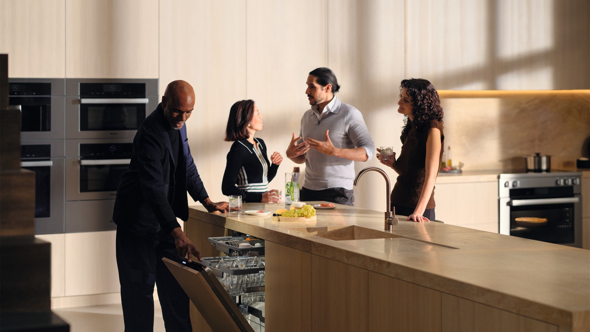 Group of friends talking around a kitchen island, while one of them opens a Miele Dishwasher to check it