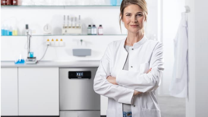 AA lab technician standing in front of a run of laboratory units. The PLW 8683 CD laboratory washer with glass door can be seen in the background.