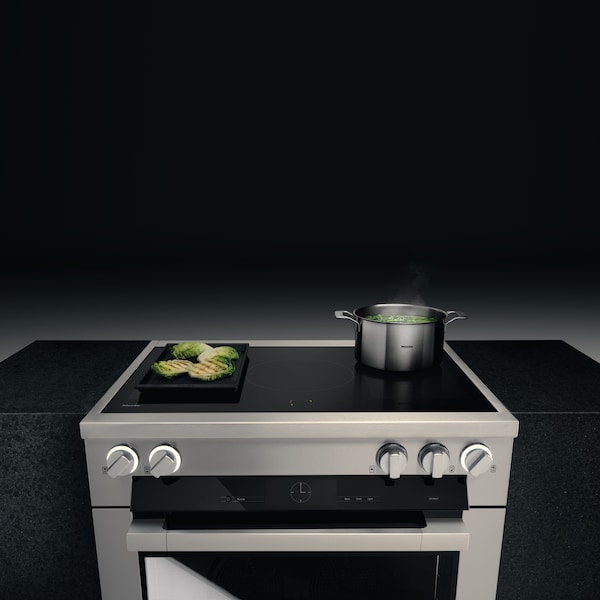 Top view of the Induction range with a pot boiling water and a pan grilling vegetables.