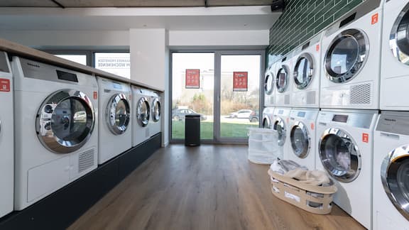 The image shows a modern laundry room equipped by appWasch with Miele Professional Little Giants washing machines and tumble dryers in a student accommodation.