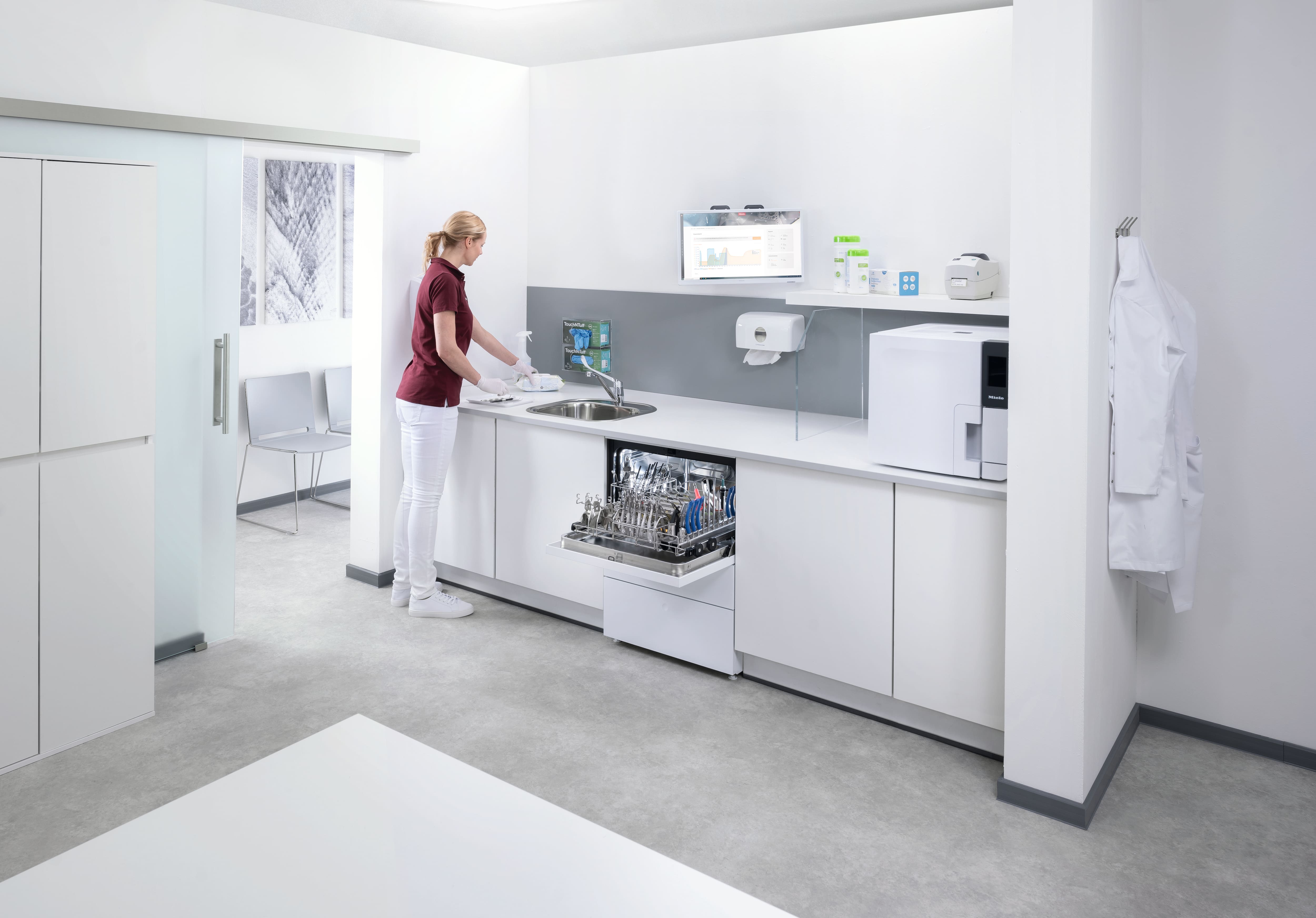 Eine Assistentin arbeitet in Instrumentenaufbereitungsräumen mit einem geöffneten und mit zahnärztlichen Instrumenten beladenen CompactLine-Thermalwaschdesinfektionsgerät.