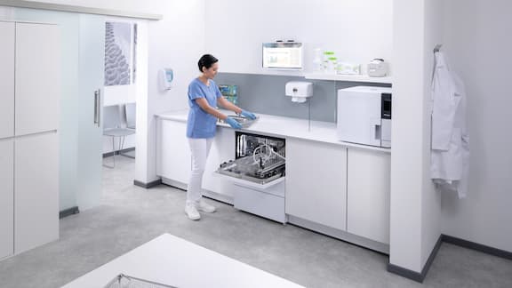 Uma assistente médica na sala de reprocessamento de instrumentos descarrega uma máquina de lavar e desinfetar CompactLine