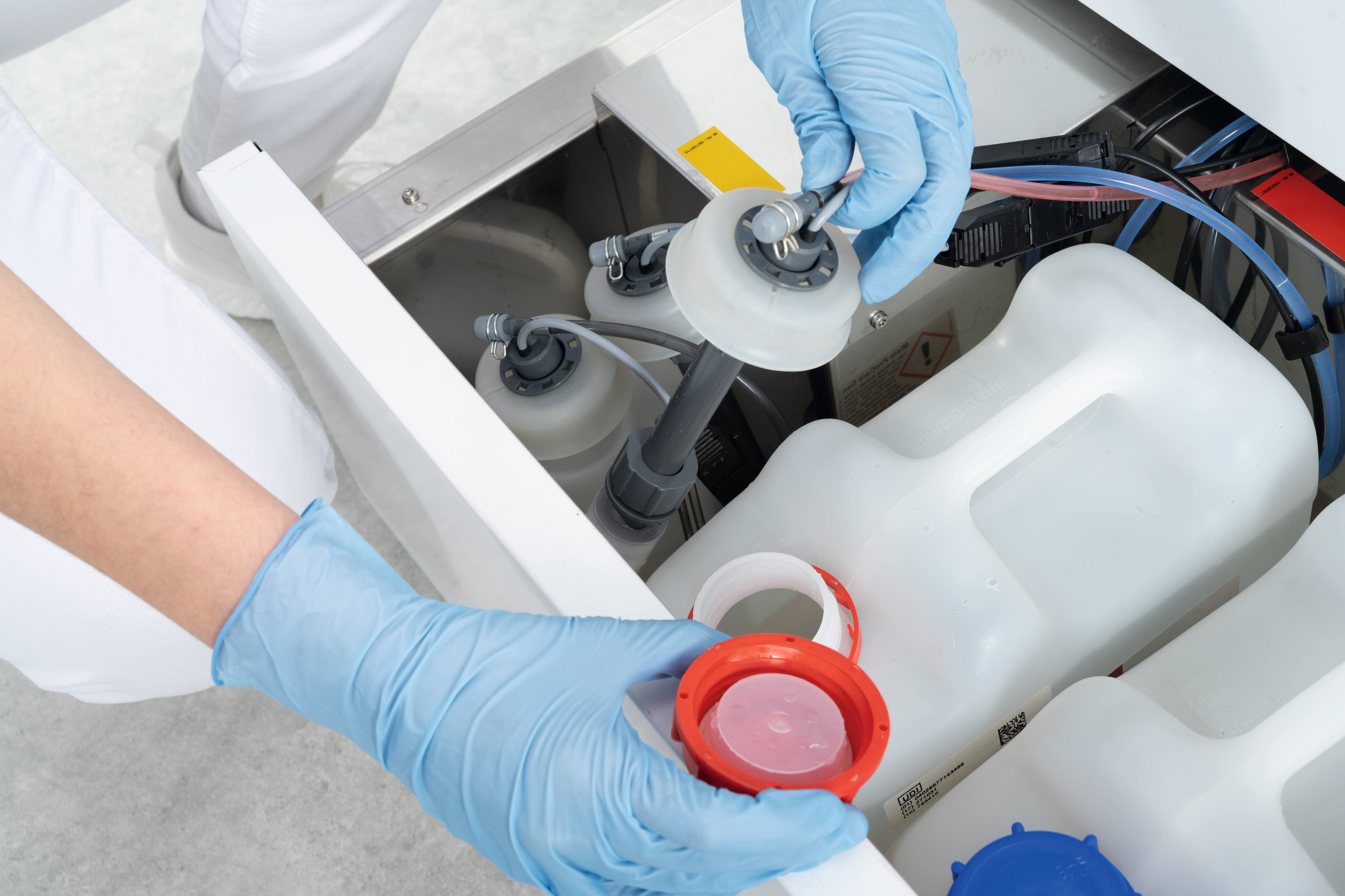 Mit Handschuhen werden die Absauglanzen und die ProCare Dent-Chemikalienbehälter in der unteren Schublade eines Miele Professional CompactLine- Thermodesinfektors gehandhabt.