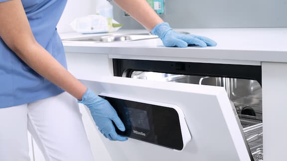 Mão com luva abre a porta de uma máquina de lavar e desinfetar CompactLine