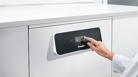 Palec dotykający czarnego wyświetlacza dotykowego wyświetlającego ikony, który jest częścią myjni laboratoryjnej wykonanej ze stali szlachetnej.