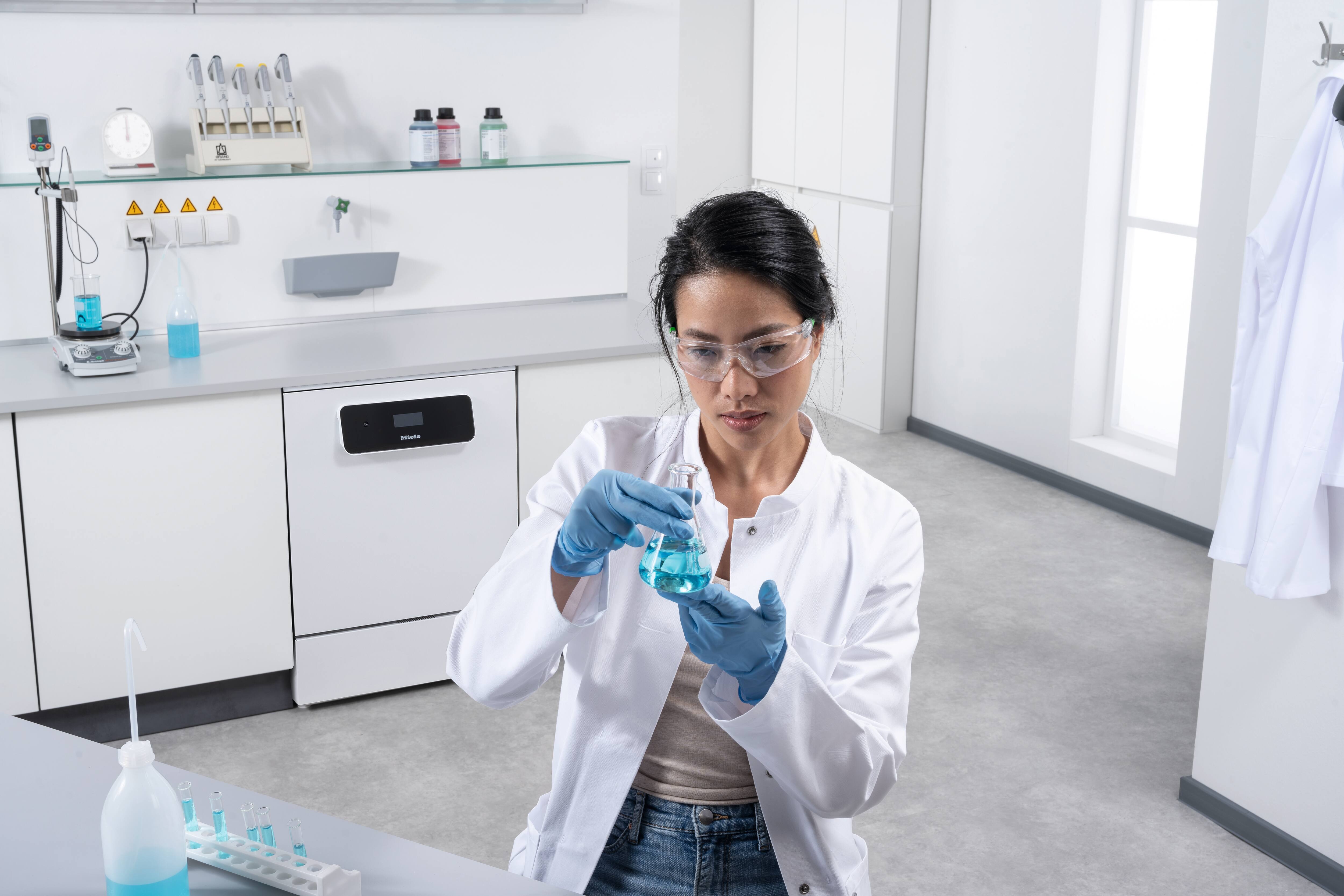 Pracovnice laboratoře stojí před laboratorní linkou. Na pozadí je vidět laboratorní myčka ExploreLine PLW 8604 v nerezovém provedení.