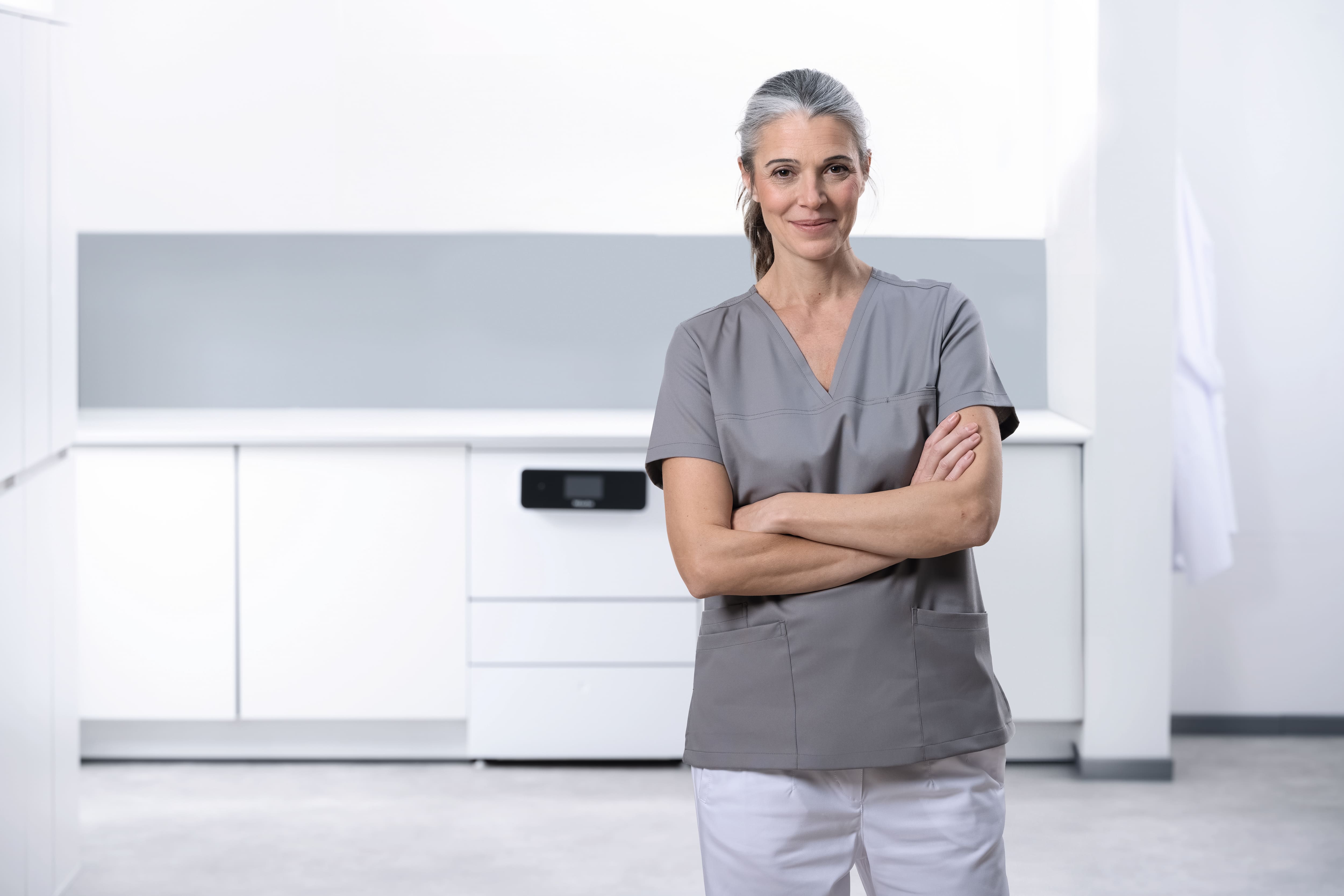 Eine medizinische Assistentin blickt in eine Kamera in einem Instrumentenaufbereitungsraum mit einem CompactLine-Reinigungs- und Desinfektionsgerät.
