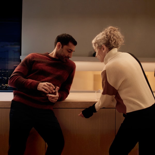 A lady, next to a man in a kitchen setting, knock on the dishwasher to open its door.