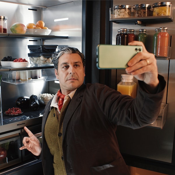 A man taking a selfie in front of a MasterCool refrigerator with its doors opened.