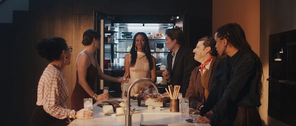 Friends eating around a kitchen island that sits in front of an opened Miele MasterCool Refrigerator