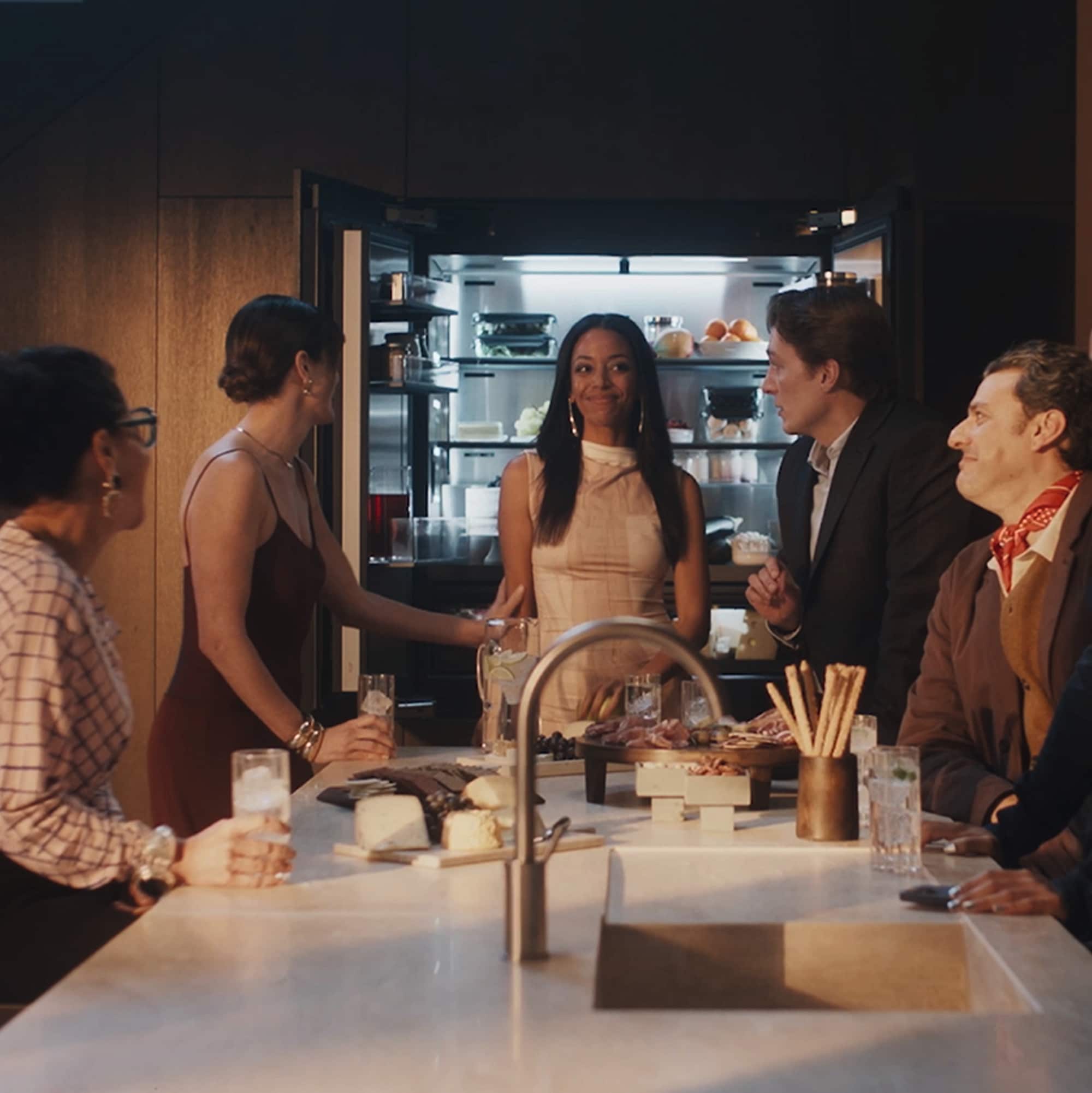 Friends eating around a kitchen island that sits in front of an opened Miele MasterCool Refrigerator