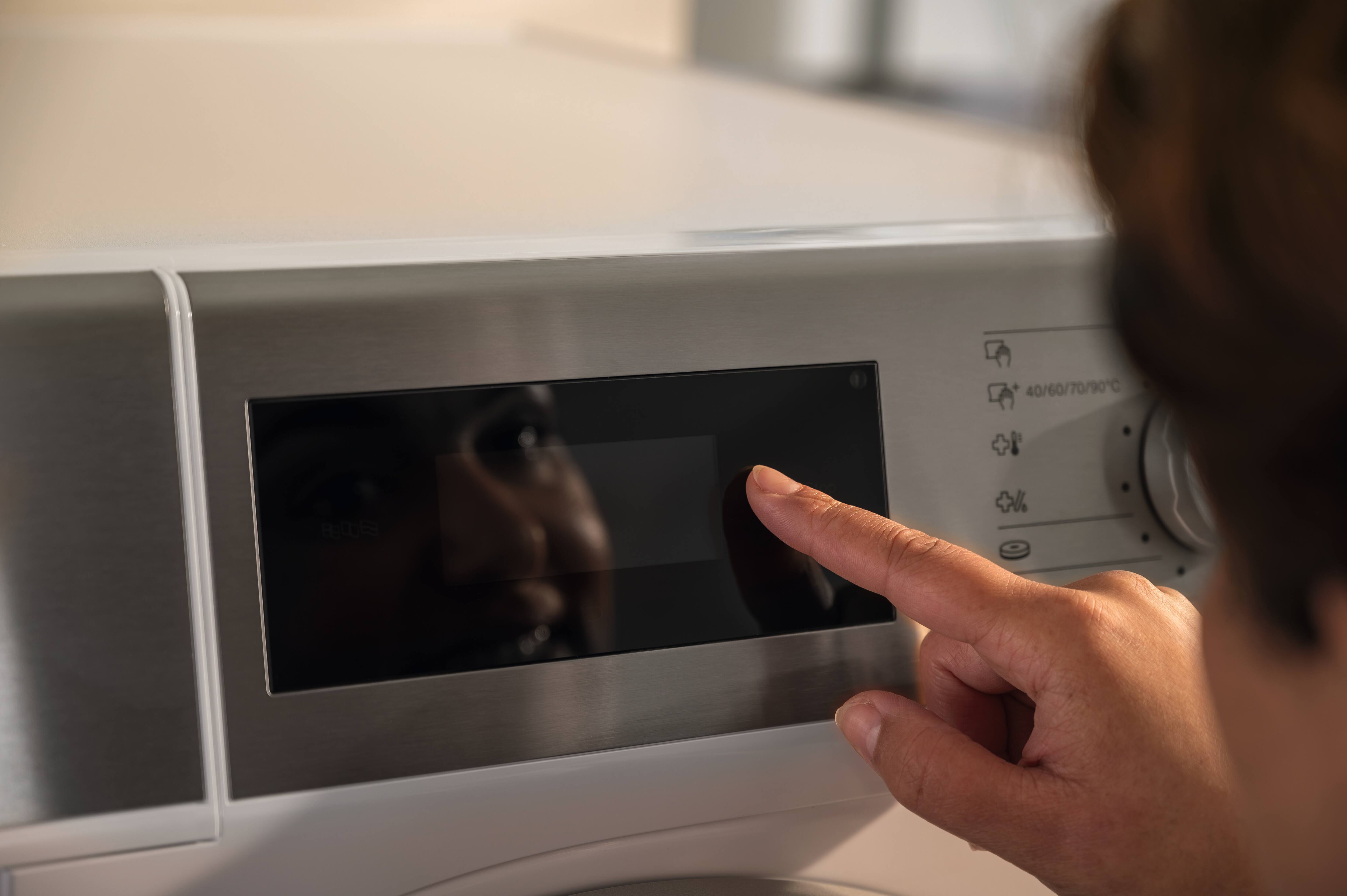 Hand bedient das Display einer Miele Kleine Riesen Waschmaschine.