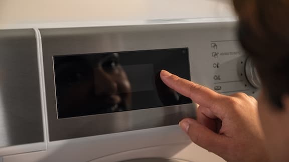 A hand operates the display of a Miele Little Giants washing machine.