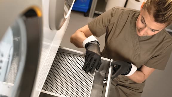 A contract cleaner employee cleans the filter of the fluff filter box in a Miele Professional Little Giants Mop Star washing machine.