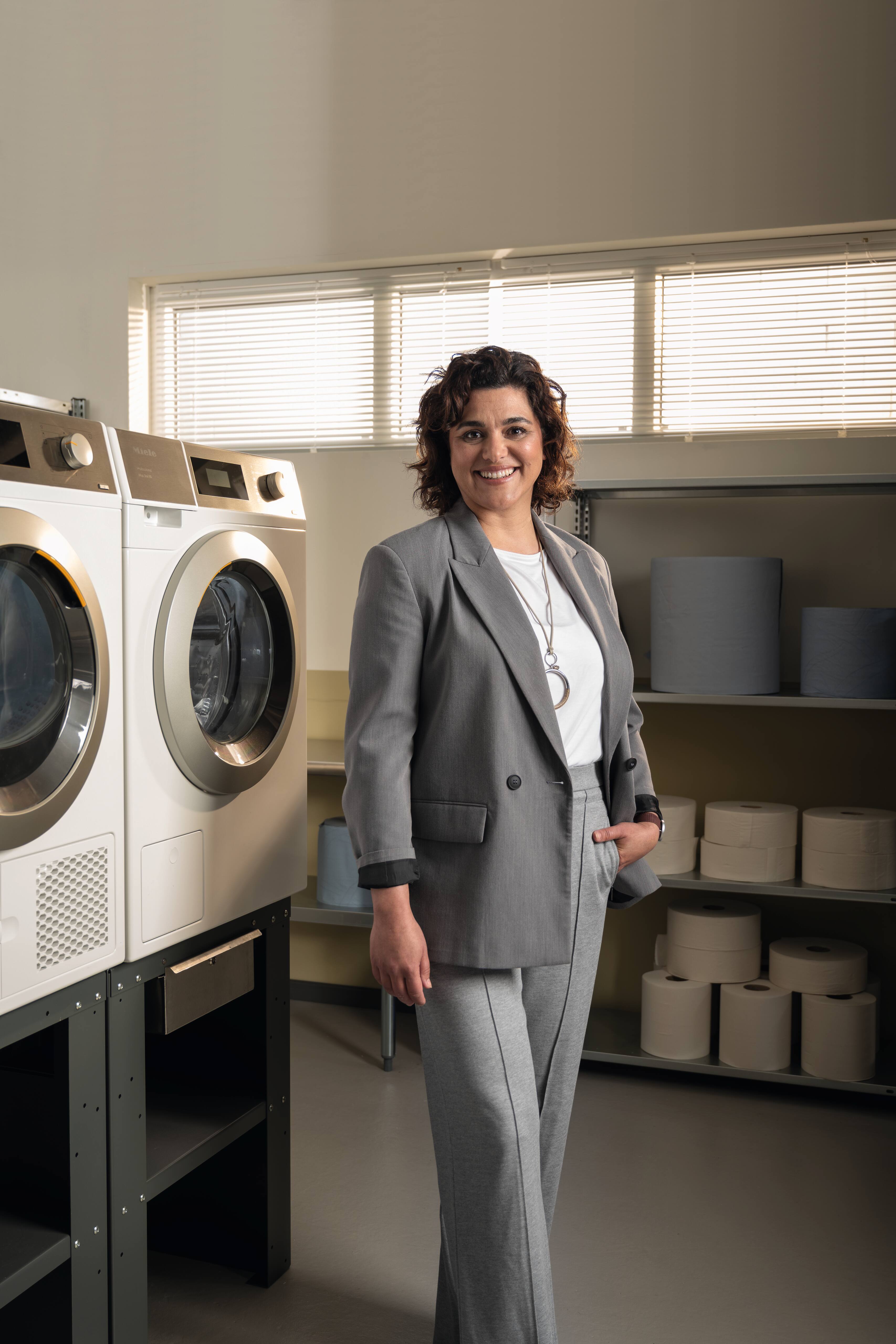 Person im Business-Outfit steht in einer professionellen Wäschereiumgebung neben Miele Kleine Riesen Maschinen.