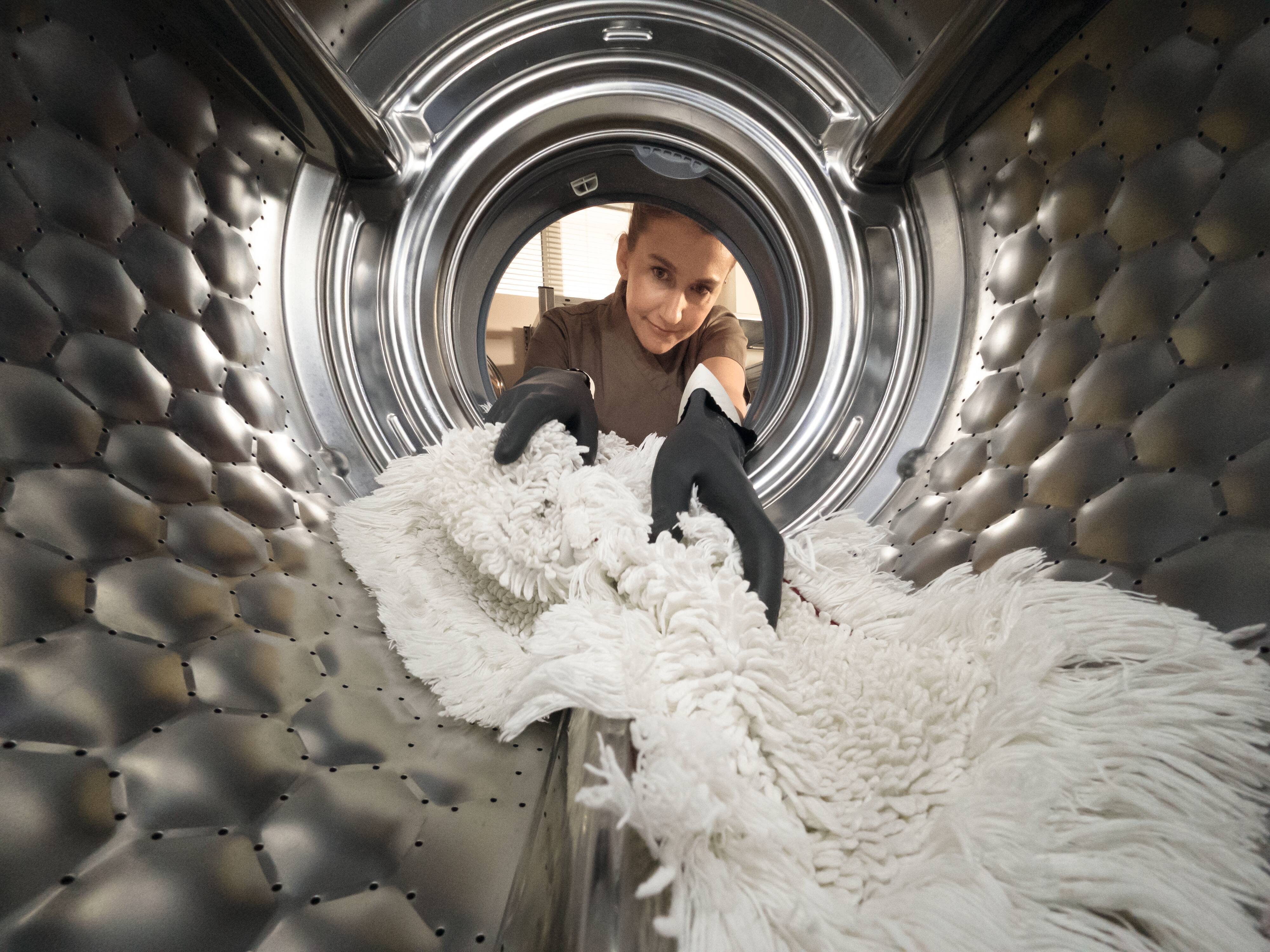  En kvinnas händer täcker en hotellsäng. Lakanen är vita. Restauranger: En anställd på en restaraunng dukar bordet.